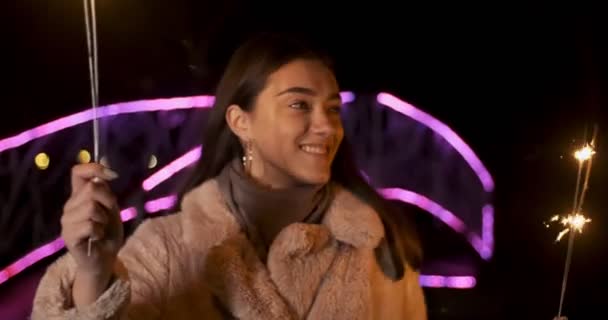 Ragazza felice modello guarda con scintille nelle loro mani. Sorridente giovane donna che celebra il nuovo anno a luci al neon sfondo. Bella femmina che si gode la celebrazione del giorno dell'indipendenza — Video Stock