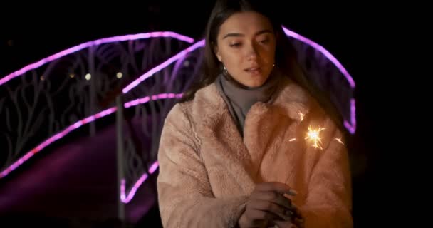 Ragazza felice modello guarda con scintille nelle loro mani. Sorridente giovane donna che celebra il nuovo anno a luci al neon sfondo. Bella femmina che si gode la celebrazione del giorno dell'indipendenza — Video Stock