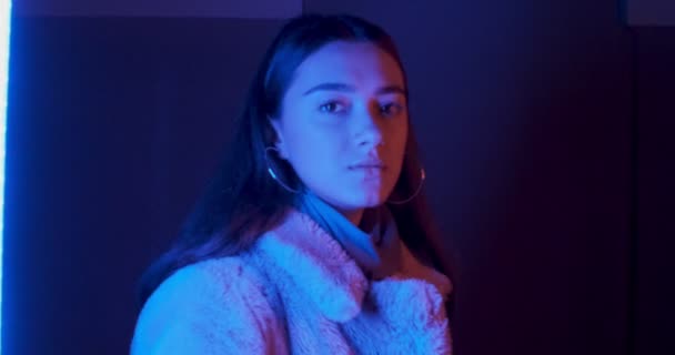 Porträt der schönen brünetten jungen Frau, die neben Neonlichtern geht und steht und fröhlich in die Kamera lächelt — Stockvideo