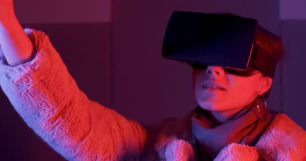 Güzel genç bayan, neon ışıklandırma arka planında sanal gerçeklik gözlüğü kullanıyor. Çekici kız sanal nesnelere VR gözlükleriyle dokunuyor. — Stok video