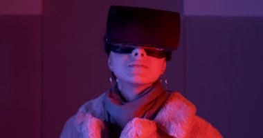 Güzel genç bayan, neon ışıklandırma arka planında sanal gerçeklik gözlüğü kullanıyor. Çekici kız sanal nesnelere VR gözlükleriyle dokunuyor.