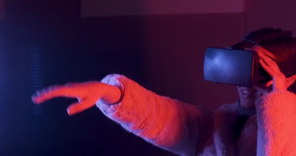Mooie jonge vrouw met behulp van virtual reality bril op neon verlichting achtergrond. Aantrekkelijk meisje aanraken virtuele objecten in vr bril — Stockvideo