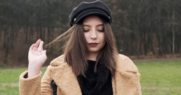 Retrato de jovem fêmea atraente que sorrindo e olhando para a câmera no gramado verde. Mulher alegremente bonita com chapéu. Fechar — Vídeo de Stock