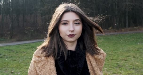 Joven chica olorosa feliz caminando sobre césped verde en el parque de otoño. Joven mujer atractiva camina y sonríe cerca del bosque — Vídeos de Stock