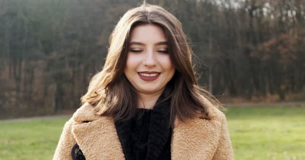 Retrato de jovem fêmea atraente que sorrindo e olhando para a câmera no gramado verde. Mulher alegremente bonita. Fechar — Vídeo de Stock