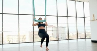 Güzel genç bir kadın büyük pencereli odada yoga egzersizi yapıyor. Hamakta vücudu ile çalışan çekici bir kadın. Rahatlama kavramı