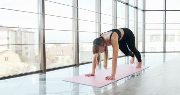 Mooie jonge vrouw doet yoga-oefeningen in de kamer met grote ramen. Aantrekkelijke vrouw die met haar lichaam werkt. Ontspanningsconcept — Stockvideo