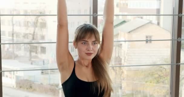 Hermosa joven haciendo ejercicio de yoga en la habitación con grandes ventanales. Atractiva mujer trabajando con su cuerpo. Concepto de relajación — Vídeos de Stock