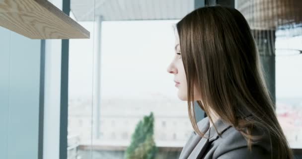Портрет молодой привлекательной девушки, смотрящей на камеру в офисе возле окна. Весело красивая женщина. Закрыть — стоковое видео
