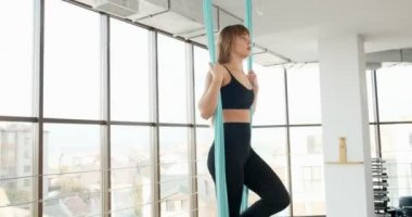Güzel genç bir kadın büyük pencereli odada yoga egzersizi yapıyor. Hamakta vücudu ile çalışan çekici bir kadın. Rahatlama kavramı