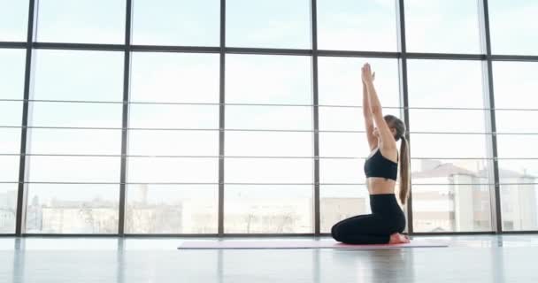 Vacker ung kvinna som motionerar yoga i rummet med stora fönster. Attraktiv kvinna som arbetar med sin kropp. Avslappningskoncept — Stockvideo