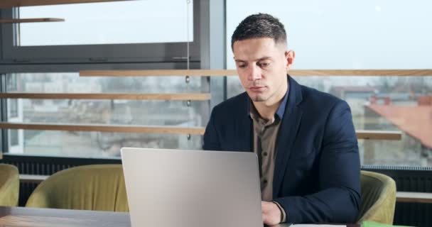 Занепокоєний чоловік працює на портативному комп'ютері і дивиться в очі, думаючи вирішити проблему в офісі. Серйозний атлетичний чоловік, що працює з ноутбуком — стокове відео