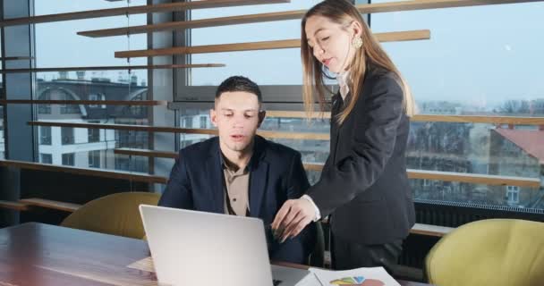 Porträt eines Mannes und einer Frau, die im hell erleuchteten modernen Büro mit Notizbuch über die Arbeit diskutieren. Betroffene Frauen erzählen arbeitenden Männern mit Laptop. Seriöse Geschäftsleute, die mit Notebooks arbeiten — Stockvideo