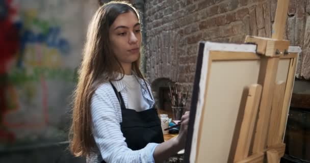 Talentvolle innovatieve mooie vrouwelijke kunstenaar tekent met borstel op het doek. Hedendaagse jonge vrouw schilder creëren abstracte beeld. Aantrekkelijk meisje creëert moderne kunst schilderen — Stockvideo