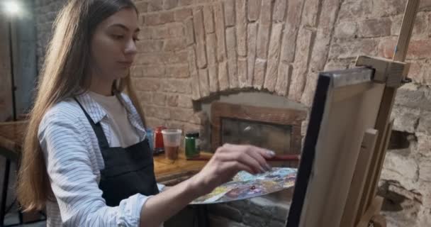 Talentosa artista femenina bonita e innovadora Dibuja con pincel en la lona. Joven pintora contemporánea creando cuadro abstracto. Muchacha atractiva crea pintura de arte moderno — Vídeos de Stock