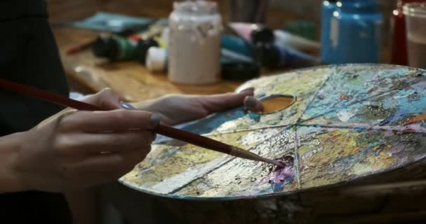 Close up of woman hand mixing oil paints on wooden palette. Attractive girl creates modern art painting. Close up female artist hand with paintbrush — Stock Video