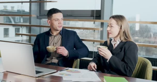 Man and a woman discussing work in the brightly lit modern office. Male and female working with laptop and drink coffee at table. Business people discuss new startup project concept — 비디오