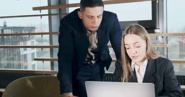 Retrato de un hombre y una mujer discutiendo el trabajo con el cuaderno en la oficina moderna brillantemente iluminada. Varón preocupado decirle a la mujer trabajadora con portátil. Gente seria de negocios que trabaja con cuaderno — Vídeos de Stock