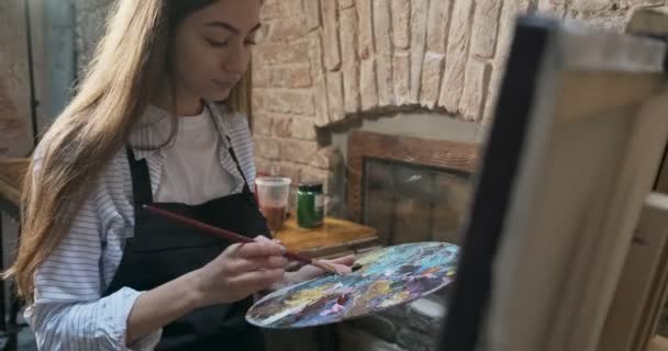 Talentosa artista femenina bonita e innovadora Dibuja con pincel en la lona. Joven pintora contemporánea creando cuadro abstracto. Muchacha atractiva crea pintura de arte moderno — Vídeos de Stock