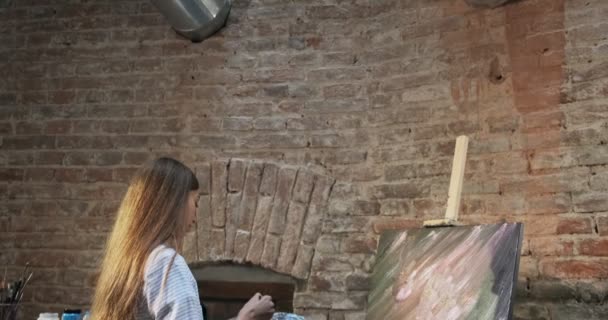 Talentvolle innovatieve mooie vrouwelijke kunstenaar tekent met borstel op het doek. Hedendaagse jonge vrouw schilder creëren abstracte beeld. Aantrekkelijk meisje creëert moderne kunst schilderen — Stockvideo