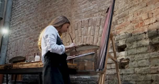 Talentvolle innovatieve mooie vrouwelijke kunstenaar tekent met borstel op het doek. Hedendaagse jonge vrouw schilder creëren abstracte beeld. Aantrekkelijk meisje creëert moderne kunst schilderen — Stockvideo