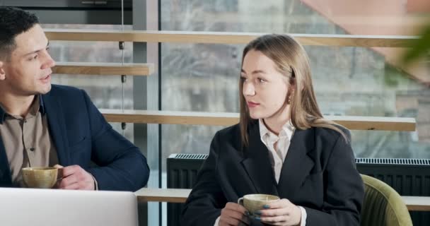 Man and a woman discussing work in the brightly lit modern office. Male and female working with laptop and drink coffee at table. Business people discuss new startup project concept — 비디오