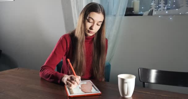 Ταλαντούχα καινοτόμα όμορφη γυναίκα σχεδιάστρια κάθεται και εργάζεται στο γραφείο. Σύγχρονη νεαρή γυναίκα που γράφει, σχεδιάζει και χρησιμοποιεί στυλό με ψηφιακή ταμπλέτα. Ελκυστική κοπέλα δημιουργεί ψηφιακές εικόνες — Αρχείο Βίντεο
