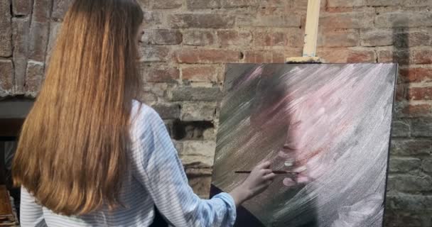 Visão traseira de talentoso inovador artista feminino bonito desenha com escova na tela. Jovem pintora contemporânea criando quadro abstrato. Menina atraente cria pintura de arte moderna — Vídeo de Stock