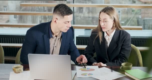 Muž a žena diskutují o práci v jasně osvětlené moderní kanceláři. Znepokojený muž a žena pracují s notebookem a mapuje papíry u stolu. Podnikatelé diskutují o novém konceptu spouštěcího projektu — Stock video