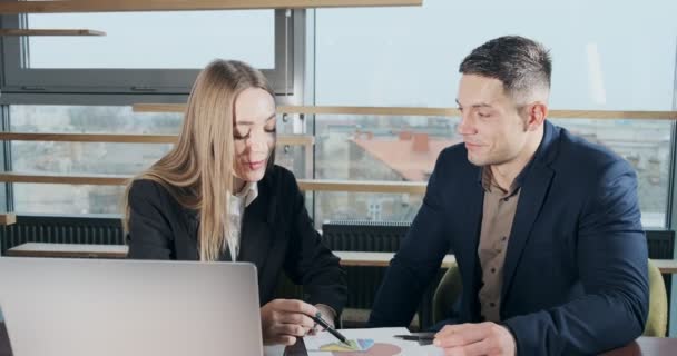 Мужчина и женщина обсуждают работу в ярко освещенном современном офисе. Обеспокоенные мужчины и женщины, работающие с ноутбуками и графиками бумаги за столом. Бизнес-люди обсуждают концепцию проекта. Передвижная камера — стоковое видео