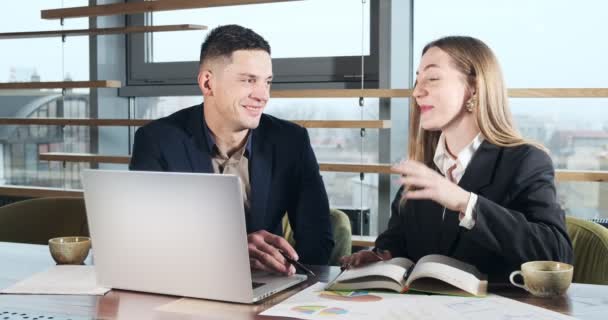 Man en vrouw praten over werk in het fel verlichte moderne kantoor. Betrokken man en vrouw werken met laptop en grafieken papieren aan tafel. Zakenmensen bespreken nieuw startup projectconcept — Stockvideo