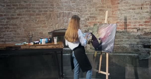 Achteraanzicht van getalenteerde innovatieve mooie vrouwelijke kunstenaar tekent met borstel op het doek. Hedendaagse jonge vrouw schilder creëren abstracte beeld. Aantrekkelijk meisje creëert moderne kunst schilderen — Stockvideo