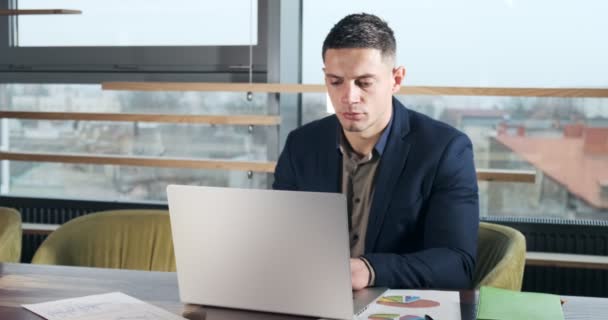 Znepokojený muž pracující na notebooku a přemýšlející o řešení problému v kanceláři. Závažný atletický muž pracující s notebookem — Stock video