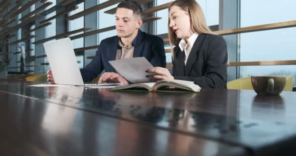 Man and a woman discussing work in the brightly lit modern office. Concerned male and female working with laptop and charts papers. Business people discuss new startup project concept. Moving camera — 비디오