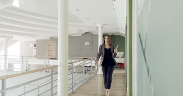 Joven mujer de negocios caminando por el pasillo de la oficina. Mujer atractiva seria va a la conferencia con cuaderno y papeles — Vídeos de Stock