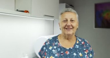 Hastanede kameraya bakıp beyaz dişlerle gülümseyen mutlu yaşlı kadın portresi.