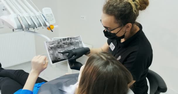 Дантист показывает молодой женщине свои зубы на рентгене — стоковое видео