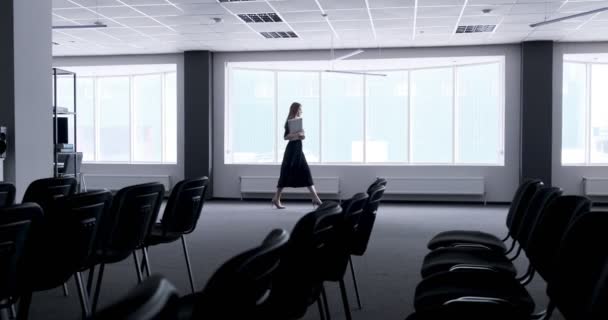 Ofis koridorunda yürüyen genç iş kadınının silueti. Ciddi çekici bir kadın defter ve kağıtlarla konferansa gidiyor. — Stok video