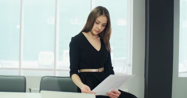 Сидя на столе, заинтересованная женщина работает и думает о решении проблемы в офисе. Серьезные привлекательные женщины, работающие с ноутбуками и бумагами — стоковое видео