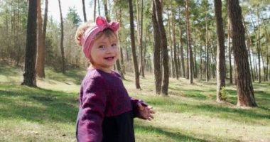 Kozalaklı ormandaki ağaçların arasında yeşil çimenlerde yürüyen mutlu küçük kız. Sosyal izolasyonda sağlıklı çocuk eğlencesi. Bahar ormanı güzelliği