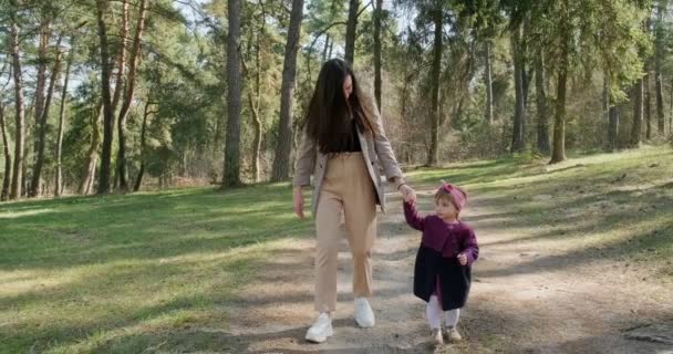 Boldog kislány sétál és játszik anyával a fák között a tűlevelű erdőben. Egészséges gyermek családi kikapcsolódás a társadalmi elszigeteltségben. Tavaszi erdő szépség — Stock videók