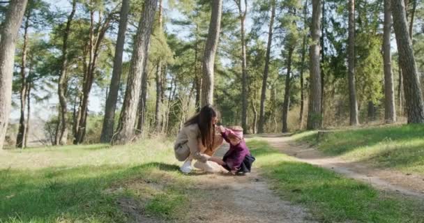 Niña feliz caminando y jugando con la madre entre los árboles en el bosque de coníferas. Recreación familiar de niños sanos en aislamiento social. Bosque de primavera belleza — Vídeo de stock