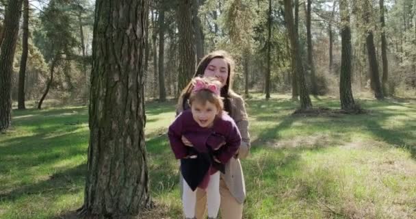 Niña feliz caminando y jugando con la madre entre los árboles en el bosque de coníferas. Recreación familiar de niños sanos en aislamiento social. Bosque de primavera belleza — Vídeo de stock