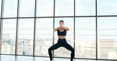 Güzel genç bir kadın büyük pencereli odada yoga egzersizi yapıyor. Vücuduyla çalışan çekici bir kadın. Rahatlama kavramı