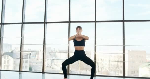 Mulher bonita fazendo exercício de ioga na sala com grandes janelas. Uma mulher atraente a trabalhar com o corpo. Conceito de relaxamento — Vídeo de Stock