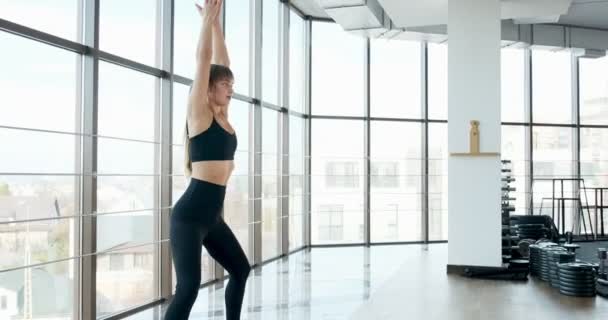 Hermosa joven haciendo ejercicio de yoga en la habitación con grandes ventanales. Atractiva mujer trabajando con su cuerpo. Concepto de relajación — Vídeo de stock