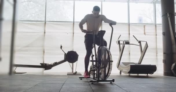 用高强度的有氧自行车训练，在密闭的体育馆里锻炼。男子做困难的有氧运动与空气自行车 — 图库视频影像