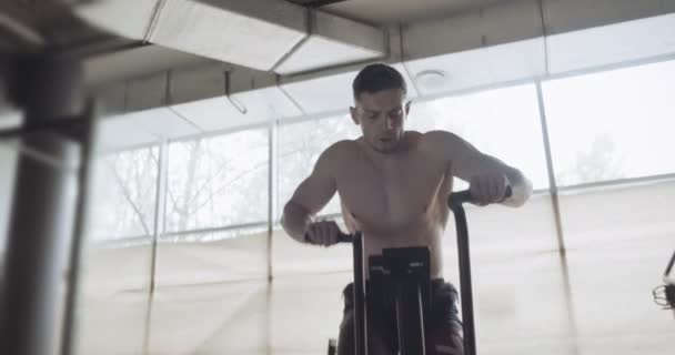 Trainen met een intense cardiotrainer, trainen in een gesloten fitnessruimte. Mannen doen moeilijke cardiotraining met de airbike — Stockvideo