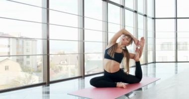 Güzel genç bir kadın büyük pencereli odada yoga egzersizi yapıyor. Vücuduyla çalışan çekici bir kadın. Rahatlama kavramı