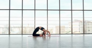 Güzel genç bir kadın büyük pencereli odada yoga egzersizi yapıyor. Vücuduyla çalışan çekici bir kadın. Rahatlama kavramı